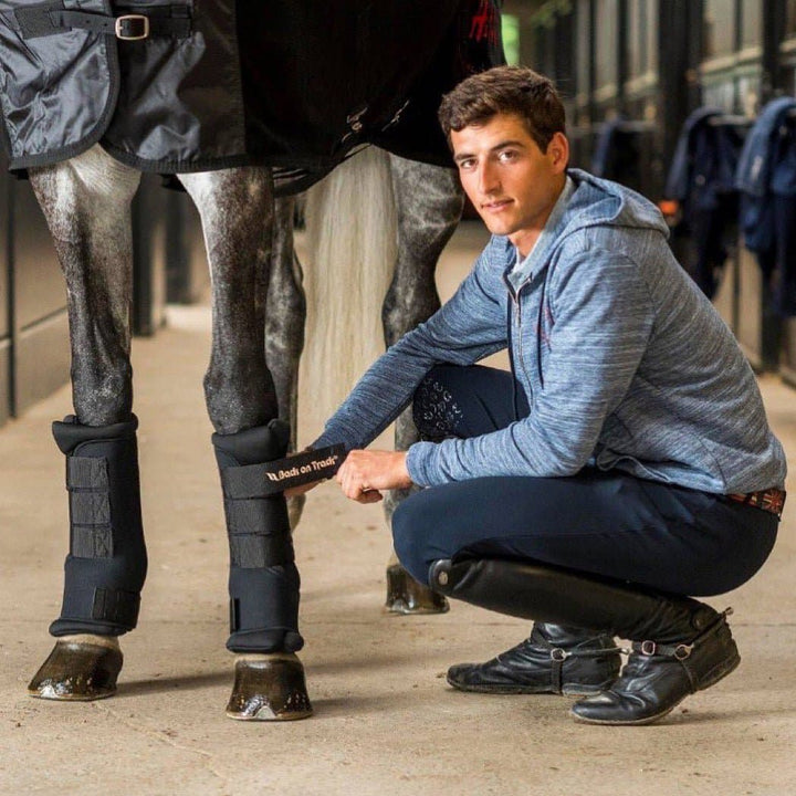 Back On Track Royal Quick Wraps being applied to a horse's legs by a person in a stable. Ideal for reducing swelling and providing leg therapy.