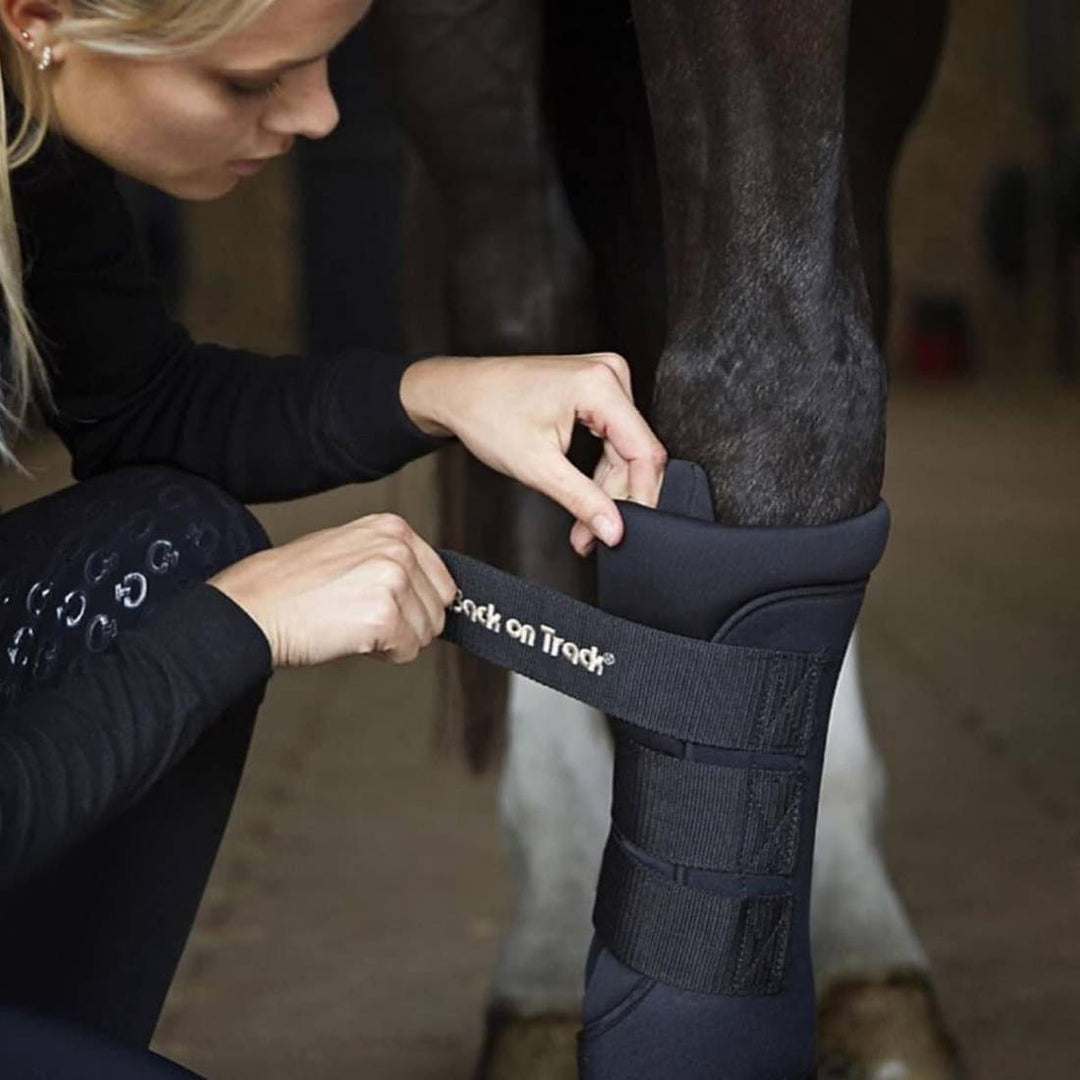 Back On Track Royal Quick Wraps being applied to a horse's leg by a person in a stable. Ideal for reducing swelling and providing leg therapy.