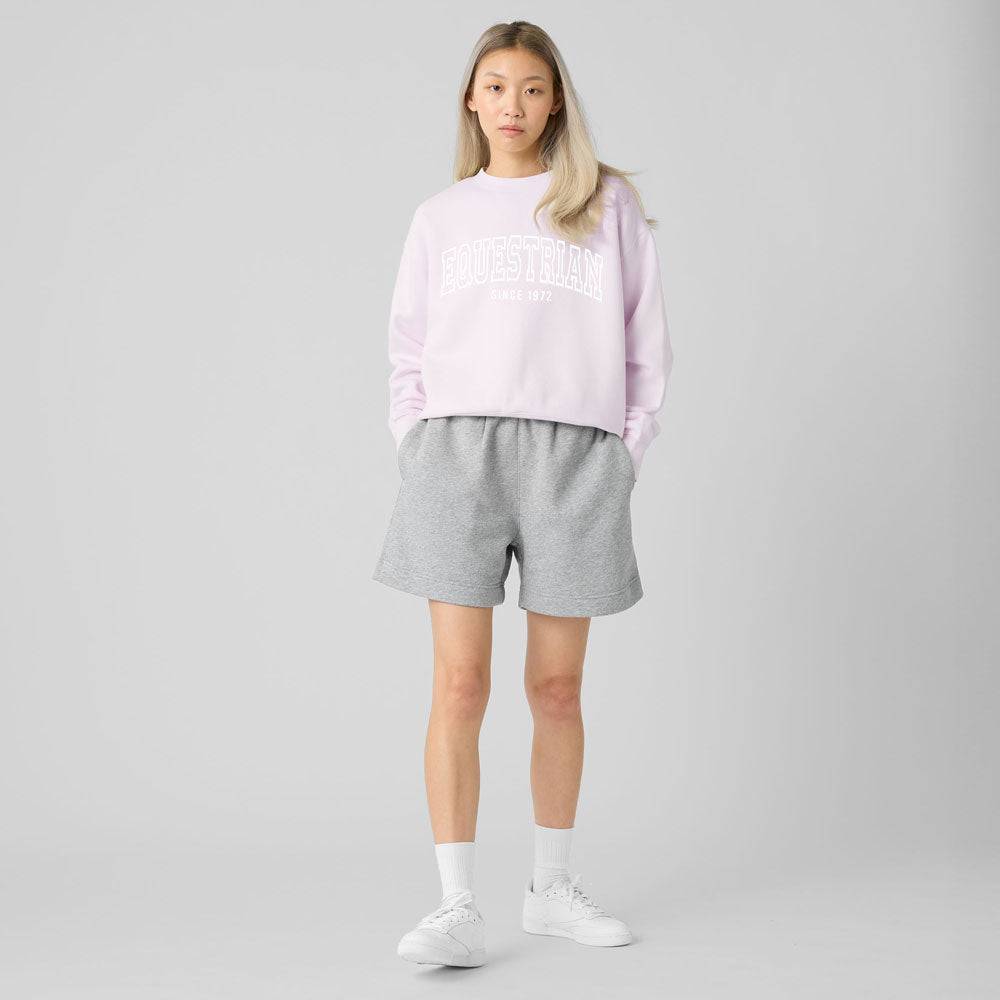 Model wearing a pastel pink Limited Edition Equestrian Sweatshirt paired with gray shorts, showcasing a casual relaxed fit.