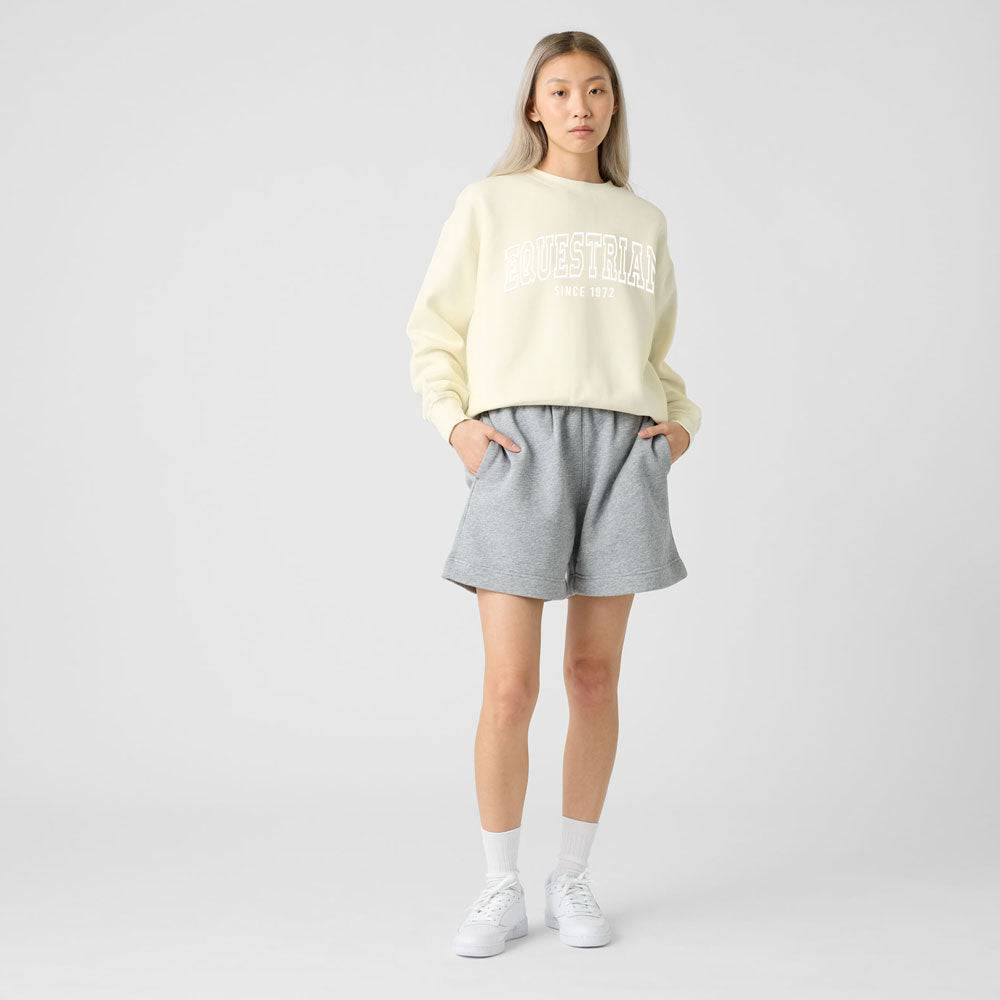 Model wearing a beige Limited Edition Equestrian Sweatshirt styled with gray shorts, highlighting its casual and relaxed design.