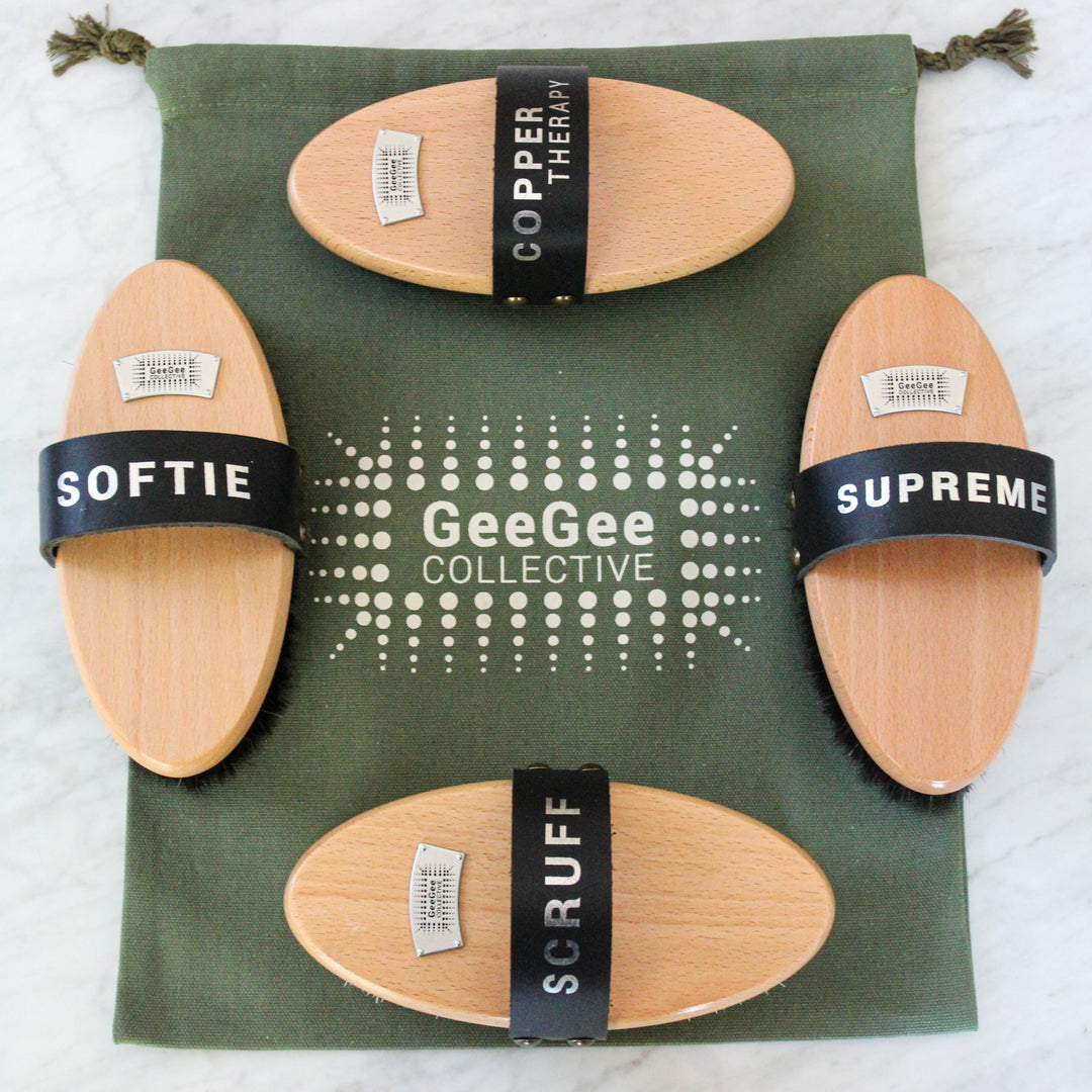 Luxury Brush Kit with four premium horse grooming brushes labeled Scruff, Copper Therapy, Dazzle, and a Softie brush, displayed on a green GeeGee Collective bag.