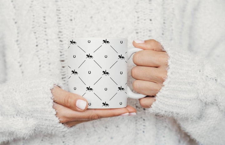 Close-up of hands holding the Dressage Diva Mug with a black equestrian and horseshoe pattern. Stylish 11oz ceramic mug for hot and cold drinks.