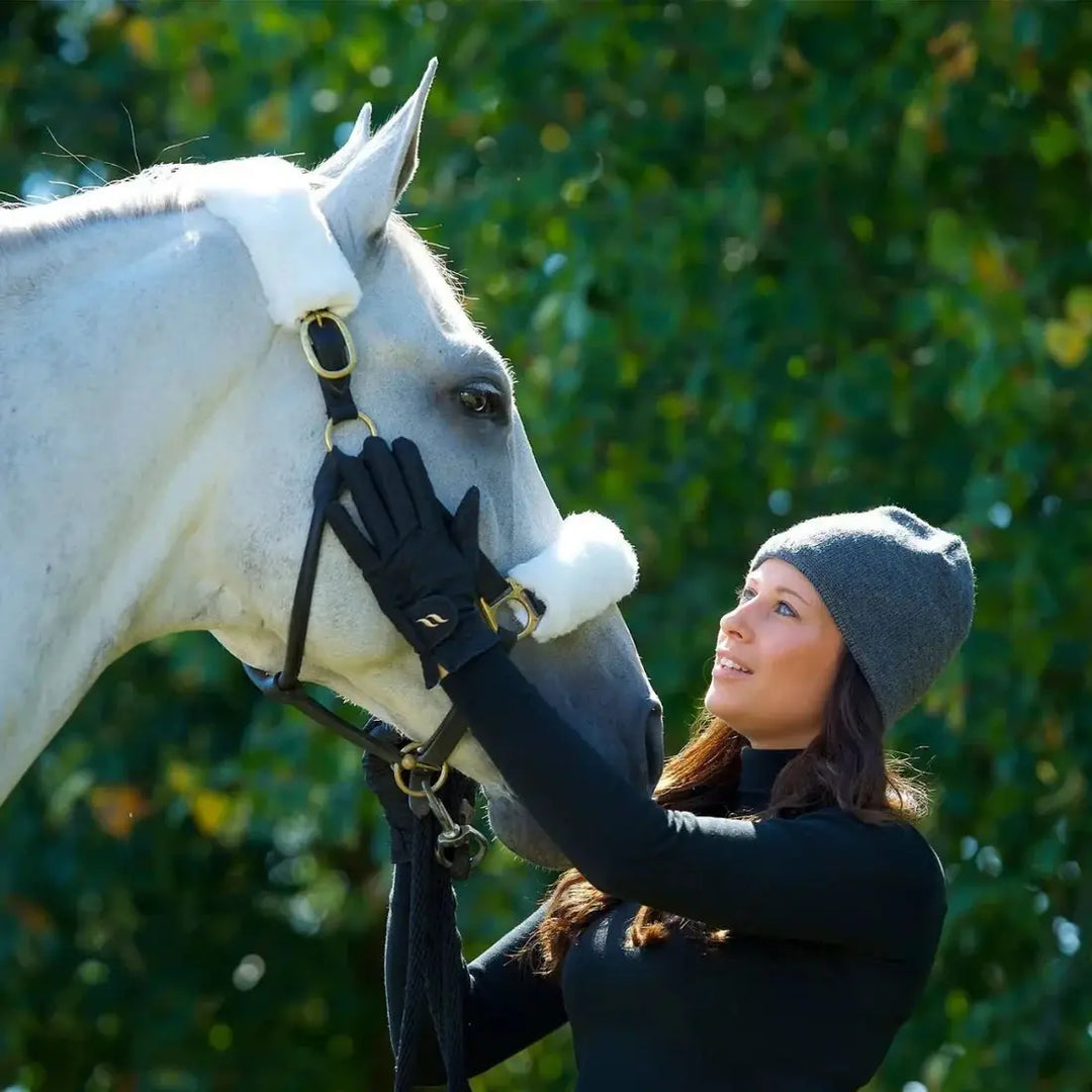 Woman wearing black therapeutic horse riding gloves while petting a white horse, highlighting equestrian use and comfort.