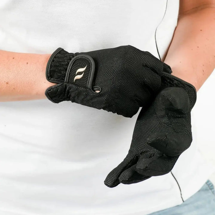 Person adjusting black therapeutic horse riding gloves with textured surface and secure strap for a snug fit.