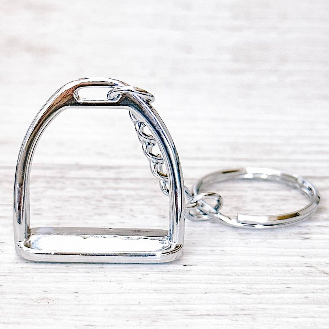 Side view of a silver stirrup keychain highlighting the smooth metallic stirrup charm and sturdy keyring.