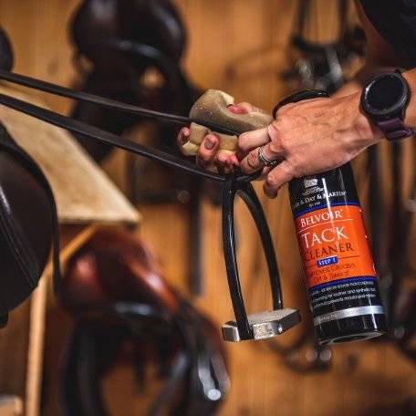 Close-up of Belvoir Step 1 Tack Cleaner Spray being applied to a leather stirrup strap, demonstrating its grease and dirt removal capabilities.