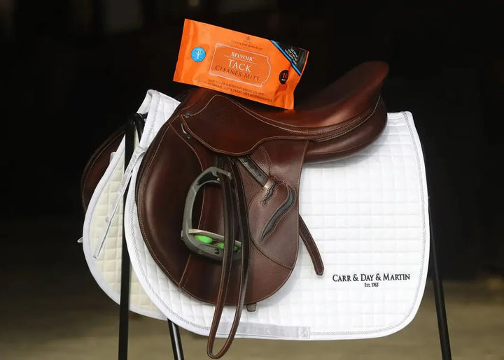 Belvoir Tack Cleaning Mitt displayed on a brown leather saddle with a white saddle pad, emphasizing its use for equestrian leather cleaning.